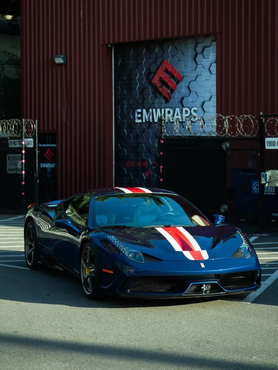 Blue Ferrari 458 Speciale with red and white stripes outside the EMWRAPS shop