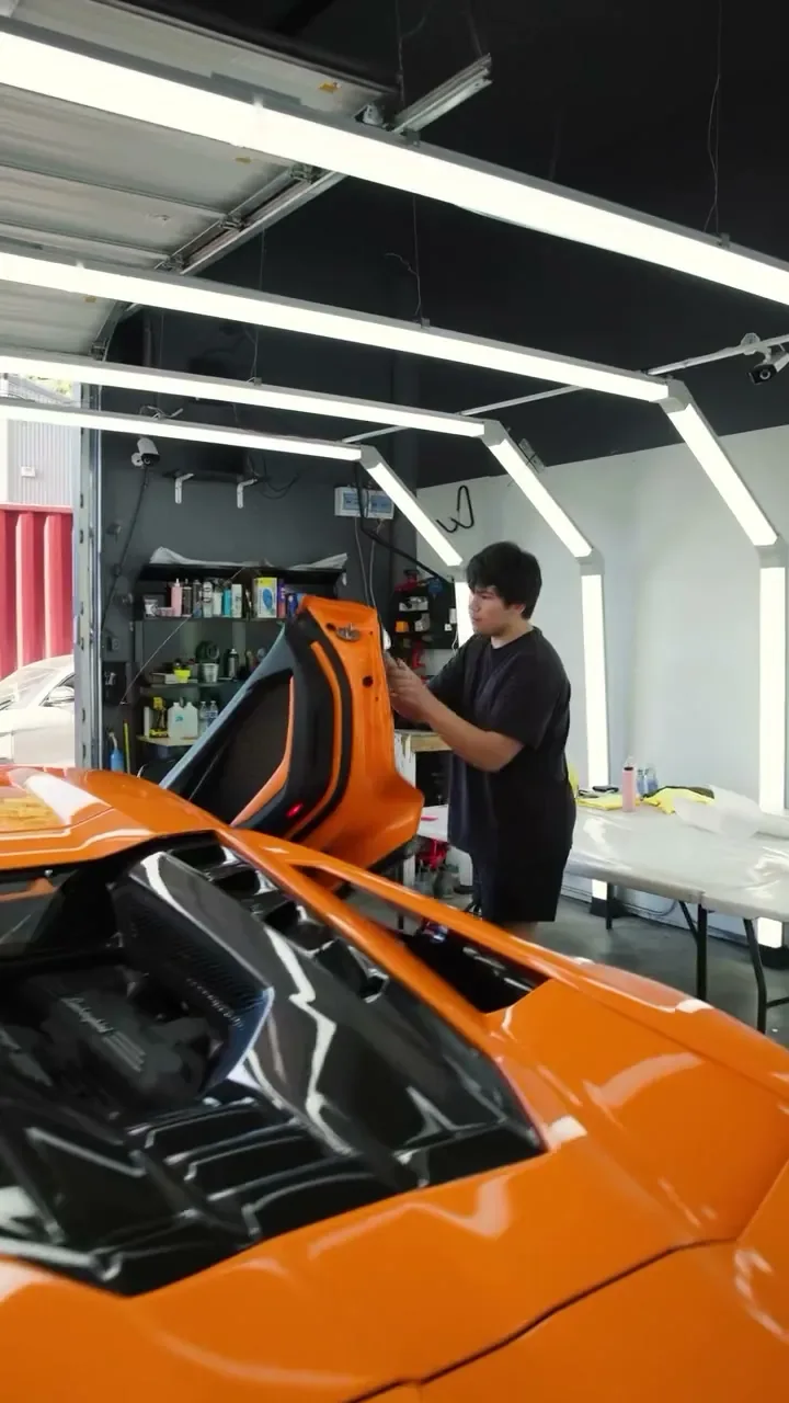 Installer fitting clear PPF to the door of an orange Lamborghini Revuelto in the EMWRAPS install bay