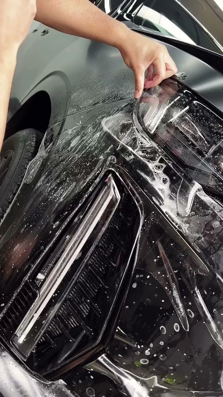 Installer laying stealth PPF over the headlight of a black Cadillac Escalade V