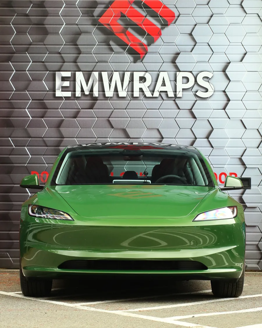 Tesla Model 3 in Champion Green color PPF in front of the EMWRAPS wall