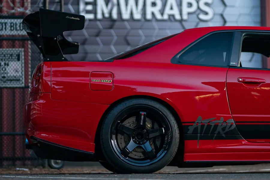 Red Nissan Skyline GT-R R34 with a black color PPF side stripe livery outside the EMWRAPS shop
