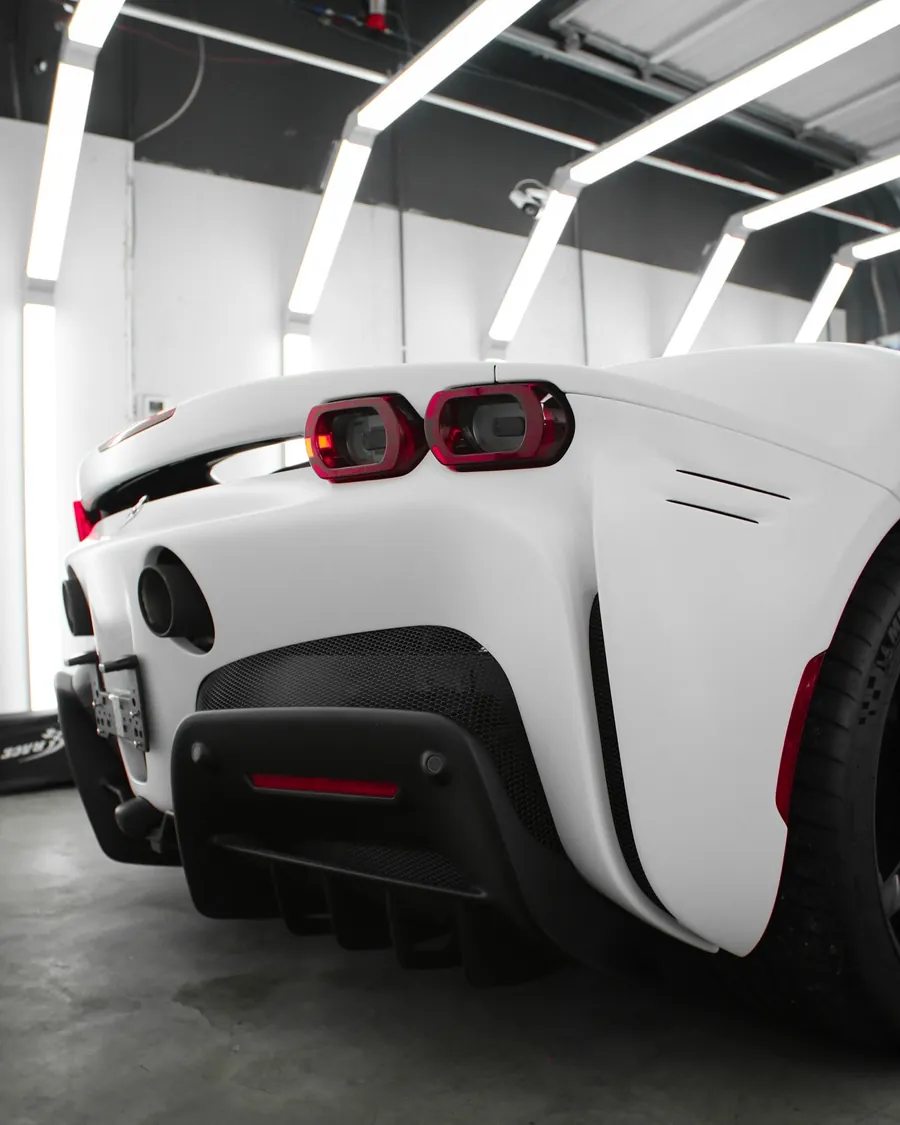 White Ferrari SF90 in satin stealth PPF in the EMWRAPS install bay, rear three-quarter view