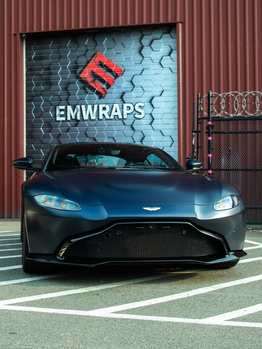 Blue Aston Martin Vantage in satin stealth PPF in front of the EMWRAPS door