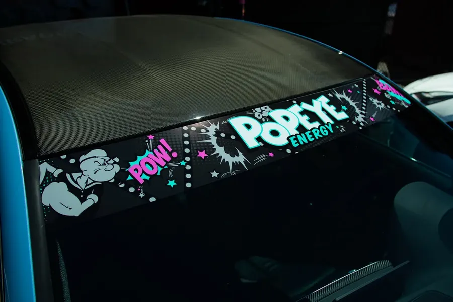 Blue BMW M4 with a printed Popeye Energy windshield banner at the EMWRAPS shop